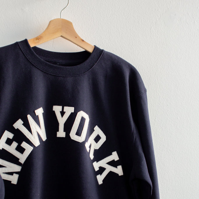 Black sweatshirt with 'New York' text on a hanger against a white background