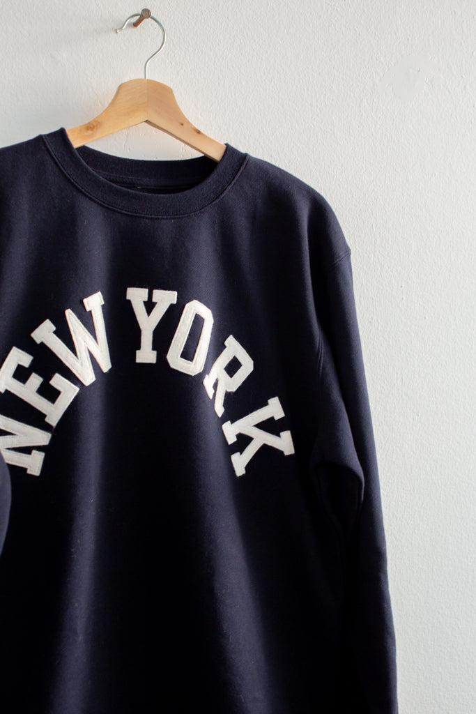 Black sweatshirt with 'New York' text on a hanger against a white background