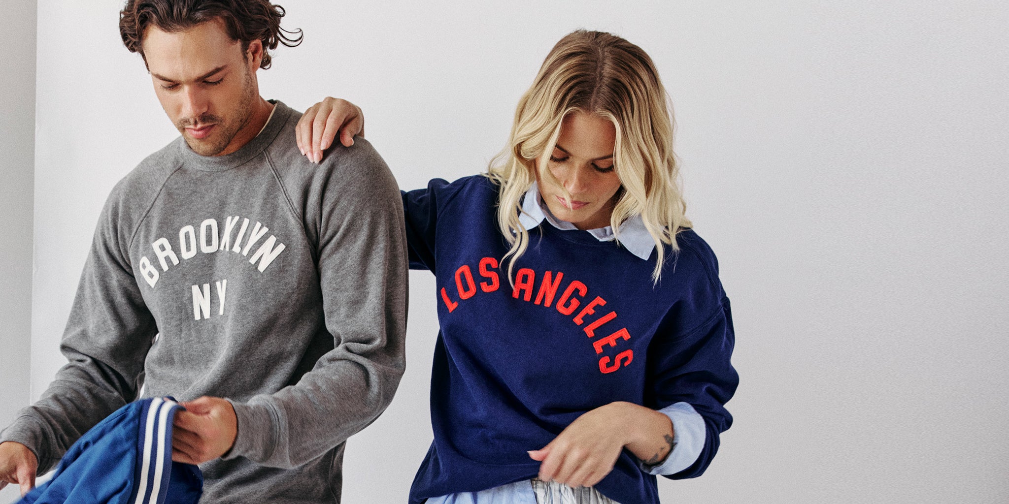 Two people wearing sweatshirts with 'Brooklyn, NY' and 'Los Angeles' text.